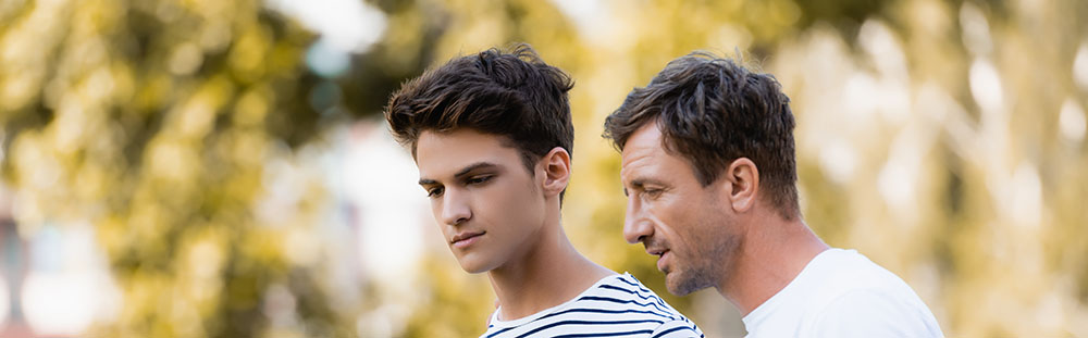 father gesturing and talking with teenager son in park