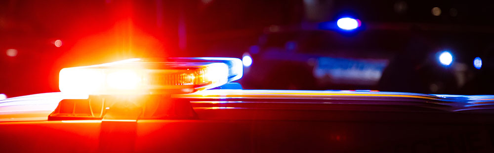 Red and blue flashing lights on police cars at a crime scene at night